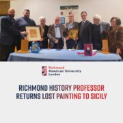 A group of people stand behind a table displaying framed artworks and a book; the image includes text about a history professor returning a painting to Sicily.